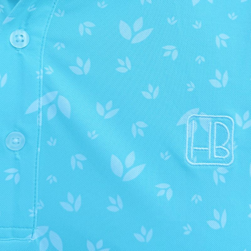 Mannequin portant un polo de golf bleu ciel Hole Black imprimé fleurs blanches aqua zoom sur le logo