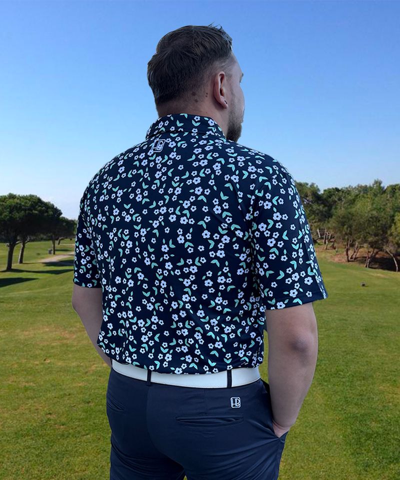 Mannequin portant un polo de golf bleu marine Hole Black imprimé Liberty fleurs blanches de dos sur un parcours de golf