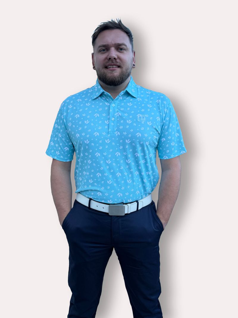 Mannequin portant un polo de golf bleu ciel Hole Black imprimé fleurs blanches aqua de face avec pantalon de golf