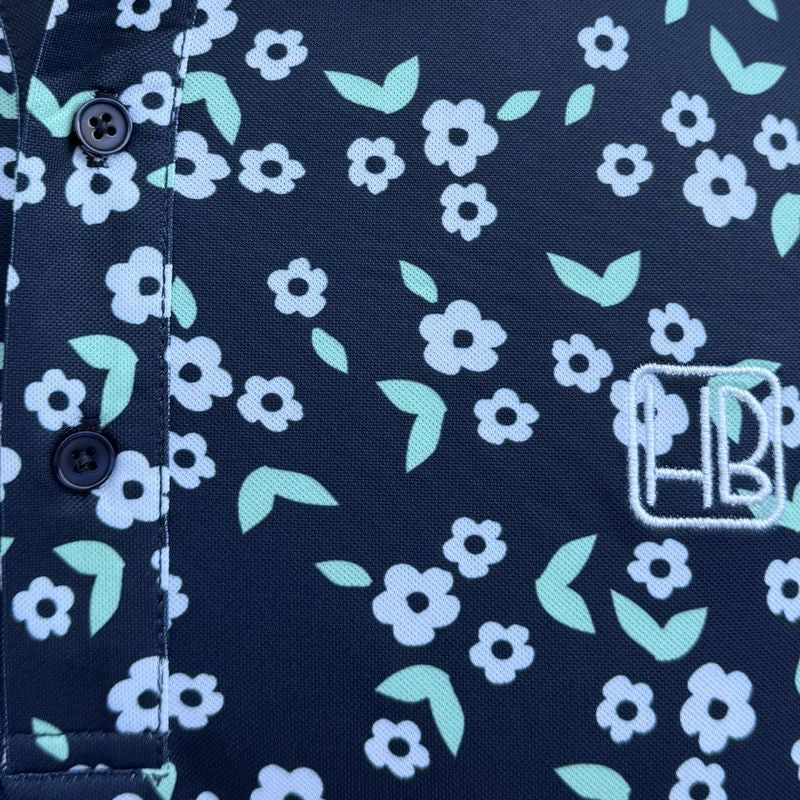 Mannequin portant un polo de golf bleu marine Hole Black imprimé Liberty fleurs blanches, zoom sur le logo