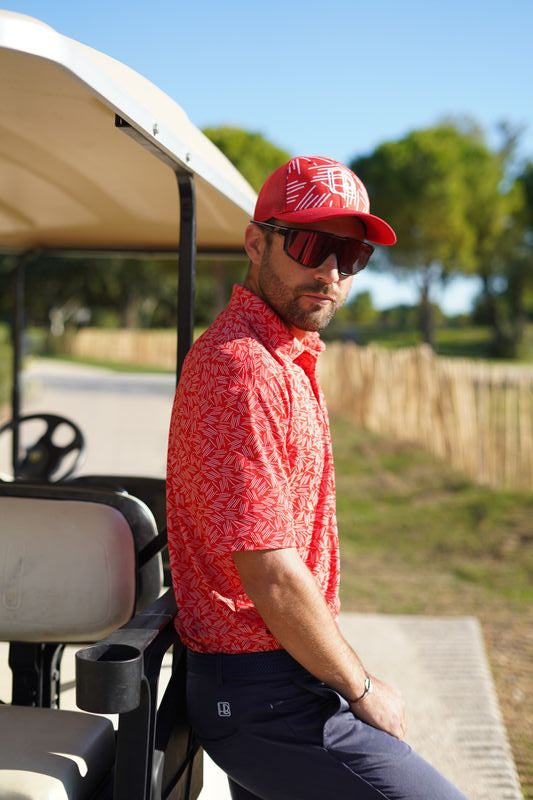 photo représentant un joueur de golf qui porte un polo de golf rouge hole black sur une voiturette