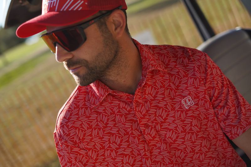 photo représentant un joueur de golf qui porte un polo de golf rouge hole black sur une voiturette